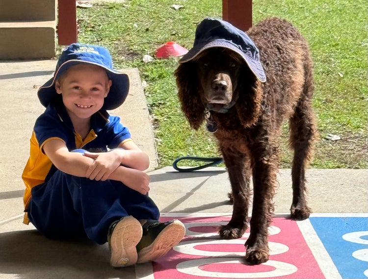 Photo of a student sitting on the ground with a support dog standing next to him