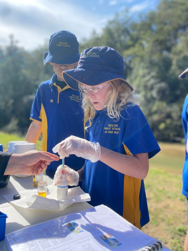 Photo of a students wearing safety goggles and gloves putting some water in a labelled science bottle with a dropper