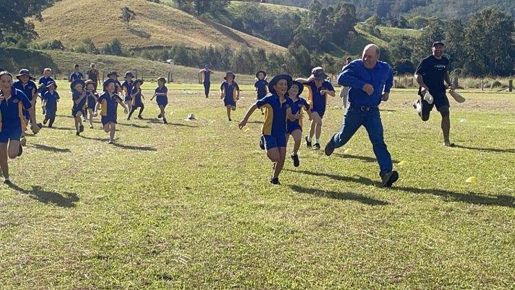 Photo of a large group of children and an adult community member running in a field