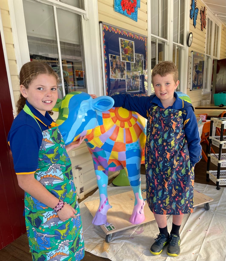 Photo of two students standing next to a painted cow statue with aprons on